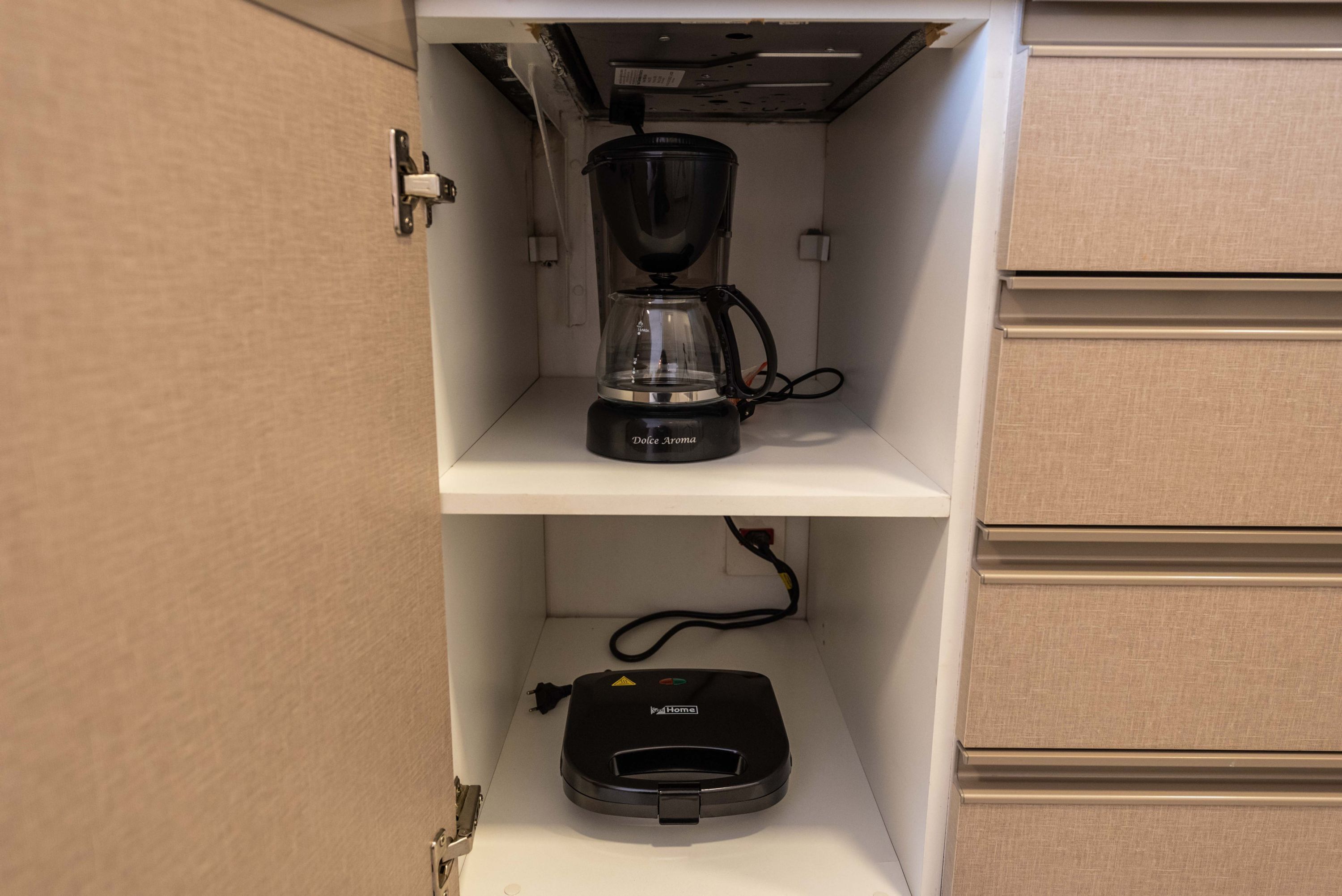 Eine Küchenzeile mit einer Kaffeemaschine auf der oberen Ablage und einem Staubsauger auf der unteren Ablage.