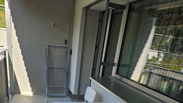 A balcony with a white table and chairs, a metal railing, and a view of a building through a window. - Parkareal Davos Vacation Rental for 2 People: Comfortable, Cozy, and Centrally Located (Davos Platz)