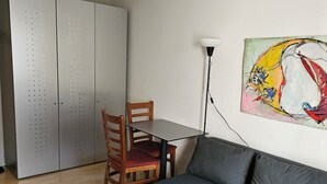A living room with a grey sofa, a wooden coffee table, a dining table with two chairs, a floor lamp, and a wardrobe with perforated doors. - Parkareal Davos Vacation Rental for 2 People: Comfortable, Cozy, and Centrally Located (Davos Platz)