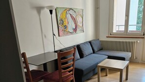 A living area with a sofa, a wooden table, a chair, and a radiator. - Parkareal Davos Vacation Rental for 2 People: Comfortable, Cozy, and Centrally Located (Davos Platz)