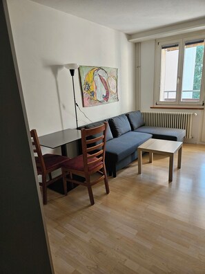 A living area with a sofa, a wooden table, a chair, and a radiator. - Parkareal Davos Vacation Rental for 2 People: Comfortable, Cozy, and Centrally Located (Davos Platz)