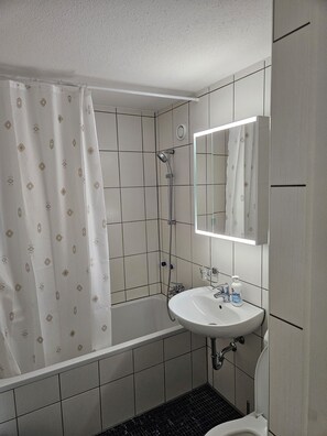 A bathroom with a bathtub, a shower, a sink, and a toilet. - Parkareal Davos Vacation Rental for 2 People: Comfortable, Cozy, and Centrally Located (Davos Platz)