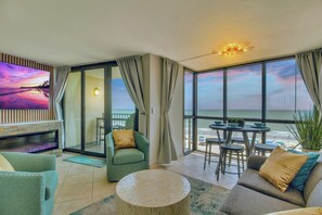Ein Zimmer mit großem Fernseher, Kamin, Balkon mit Blick auf den Strand und Essbereich mit Gartenmöbeln.