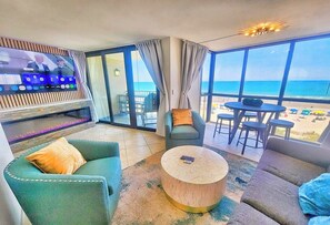 Ein Hotelzimmer mit großem Fenster, einer Sitzecke mit Sofa und Sesseln, einem kleinen runden Couchtisch und einem flachbildfernseher an der Wand.