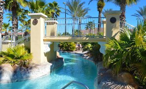 A pool area with a bridge, palm trees, and a clear sky. - Bright & Airy 4BR Disney Home w/ Patio & Parking (Davenport)