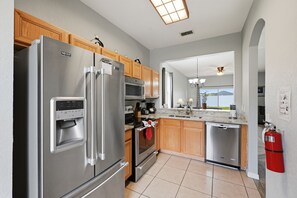 A modern kitchen with stainless steel appliances, wooden cabinets, and a large window offering a view. - Bright & Airy 4BR Disney Home w/ Patio & Parking (Davenport)