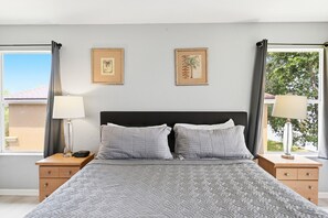 A bedroom with a bed, two bedside tables, a nightstand, two wall-mounted lamps, and two framed pictures. - Bright & Airy 4BR Disney Home w/ Patio & Parking (Davenport)