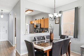 A dining area with a marble table, leather chairs, a chandelier, and a kitchen in the background. - Bright & Airy 4BR Disney Home w/ Patio & Parking (Davenport)