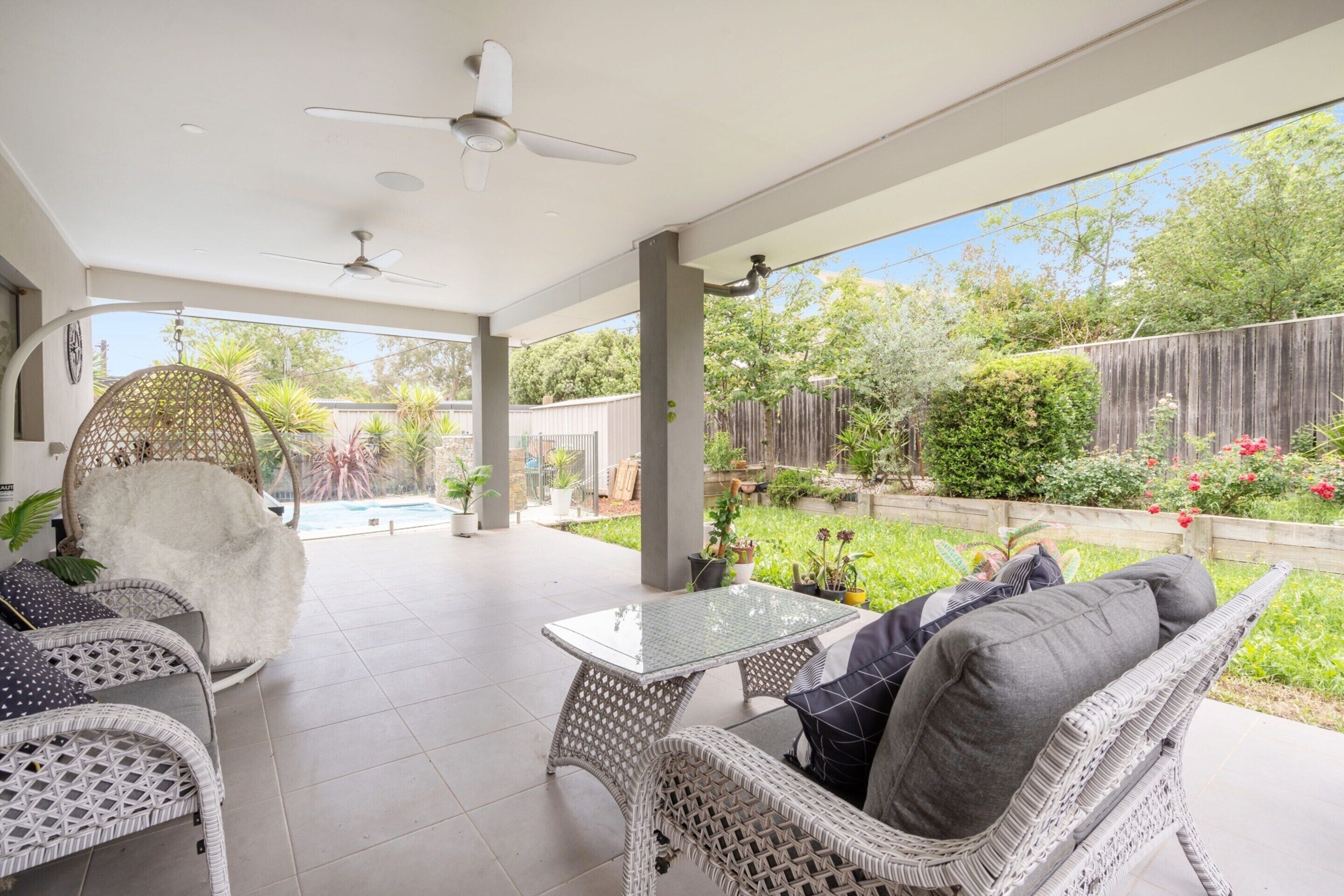 A covered patio with wicker furniture, a glass table, and a ceiling fan.