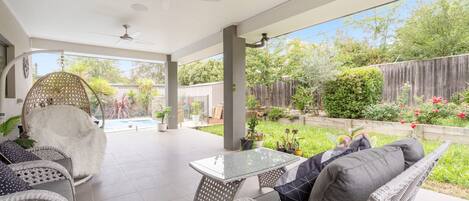 A covered patio with wicker furniture, a glass table, and a ceiling fan.