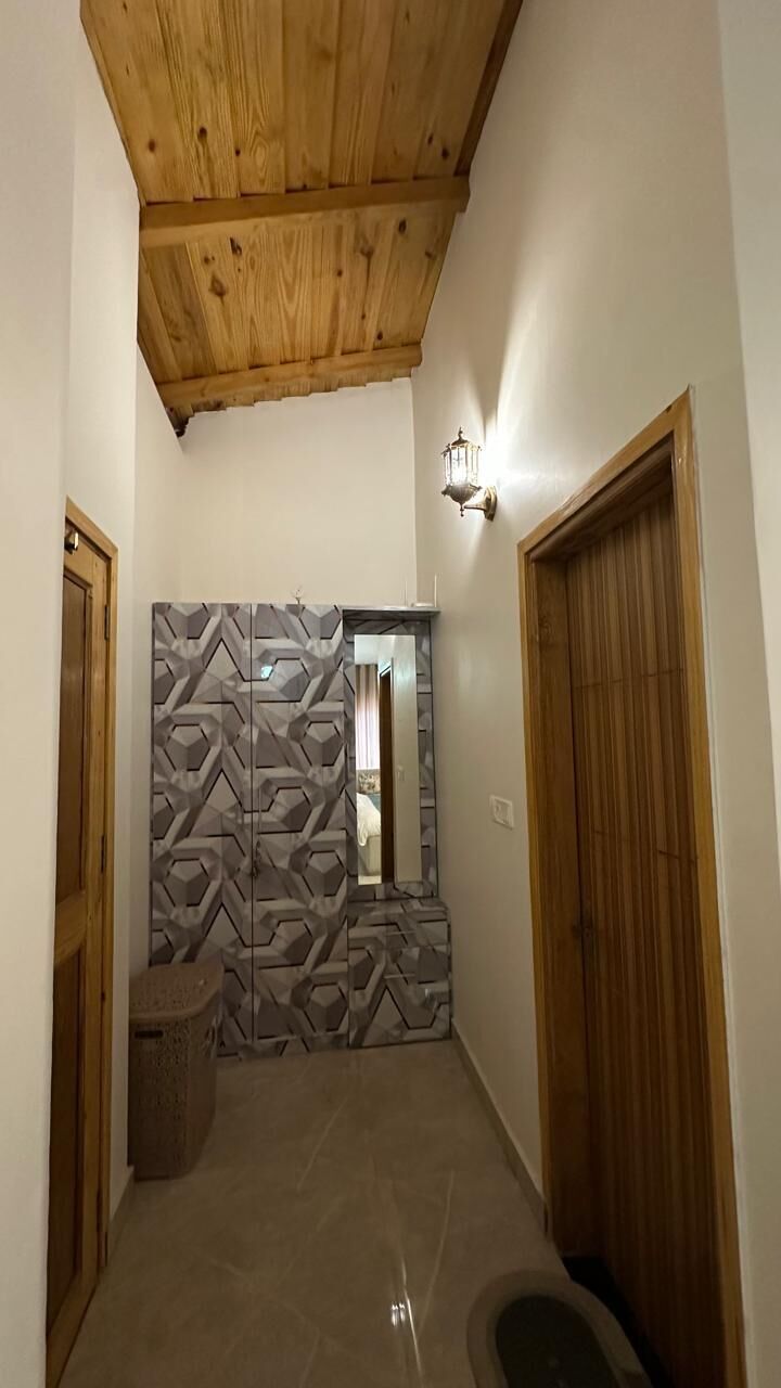 A hallway with a wooden ceiling, a geometric-patterned wall, a mirror, and a wooden door.
