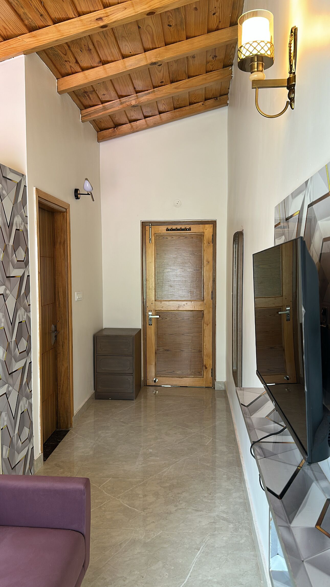 A hallway with a wooden ceiling, a door with a glass panel, a small cabinet, and a television on a stand.