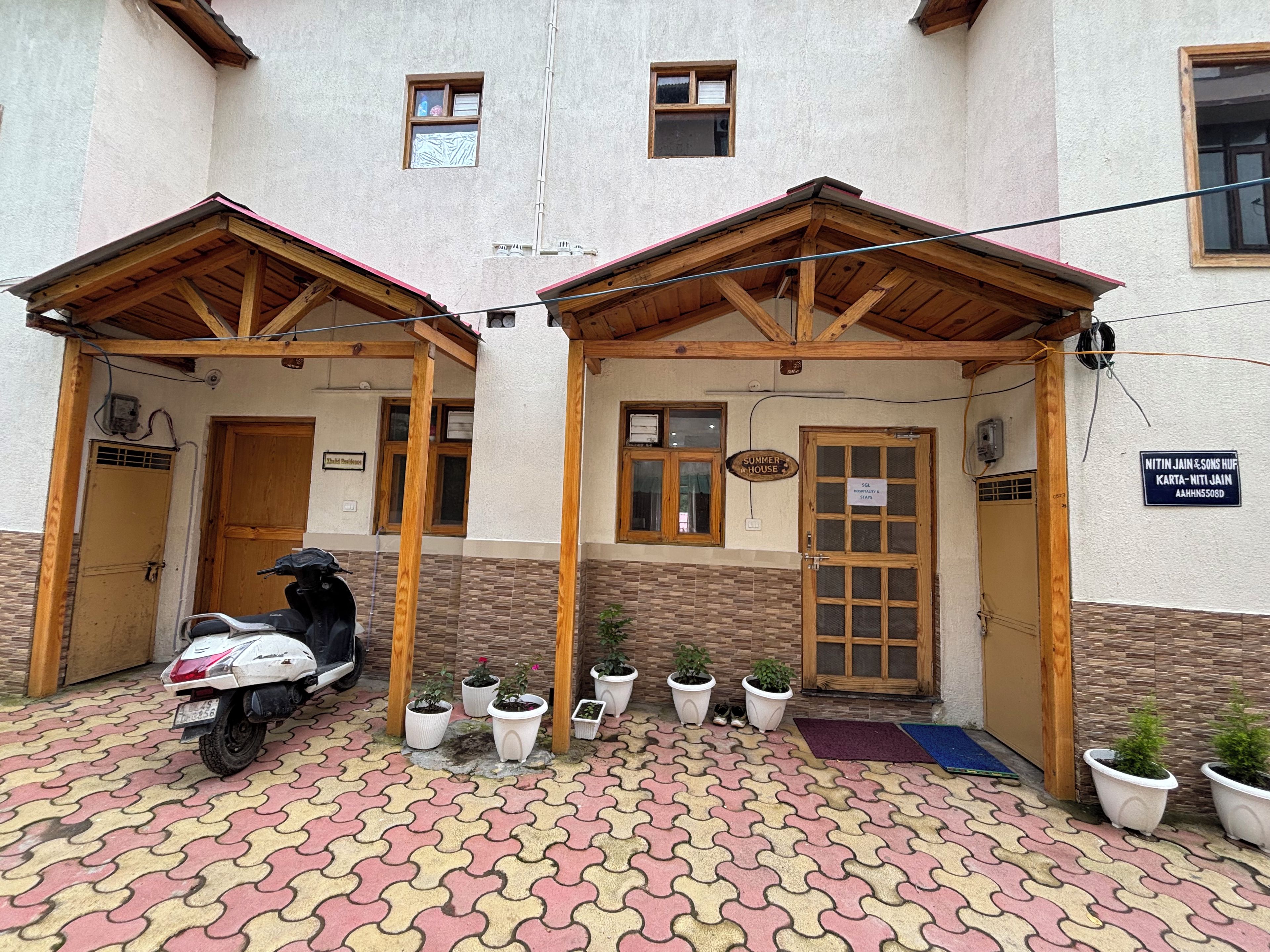 Un bâtiment doté de deux entrées abritées, avec un scooter garé à l’extérieur et plusieurs plantes en pot.