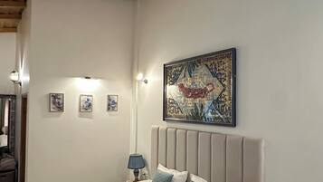 A bedroom with a wooden ceiling, a bed with white bedding and blue pillows, a bedside lamp, and a wall-mounted painting.