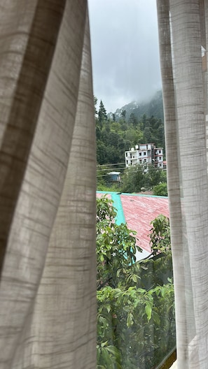 Vista a través de una ventana con cortinas, mostrando un edificio de techo rojo y un campo verde al frente.