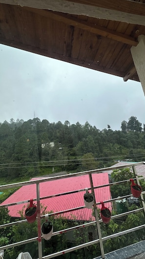Ein Balkon mit rotem Dach, Pflanzkübeln und Blick auf einen bewaldeten Hügel.