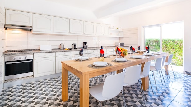 A modern kitchen with white cabinets, a built-in oven, and a dining area with a wooden table and white chairs. - Holiday villa with BBQ and heatable pool (Albufeira)