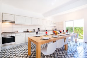 A modern kitchen with white cabinets, a built-in oven, and a dining area with a wooden table and white chairs. - Holiday villa with BBQ and heatable pool (Albufeira)