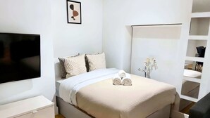 Ein modernes Schlafzimmer mit Bett, Fernseher, Nachttisch und einer festen Regalanlage.