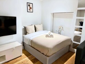 Ein modernes Schlafzimmer mit Bett, Fernseher, Nachttisch und einer festen Regalanlage.