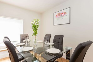 Un coin repas avec une table en verre, quatre chaises et un vase de fleurs.