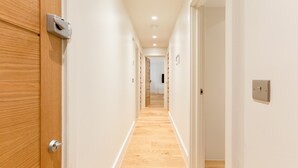 Ein Korridor mit Holztüren und weißen Wänden, der in einen Raum mit Holzboden führt.