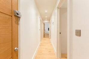 Ein Korridor mit Holztüren und weißen Wänden, der in einen Raum mit Holzboden führt.