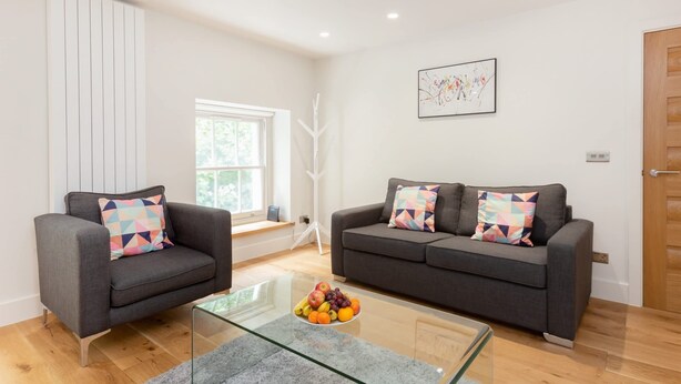Ein modernes Wohnzimmer mit zwei grauen Sofas, einem Glastisch und einer Obstschale.