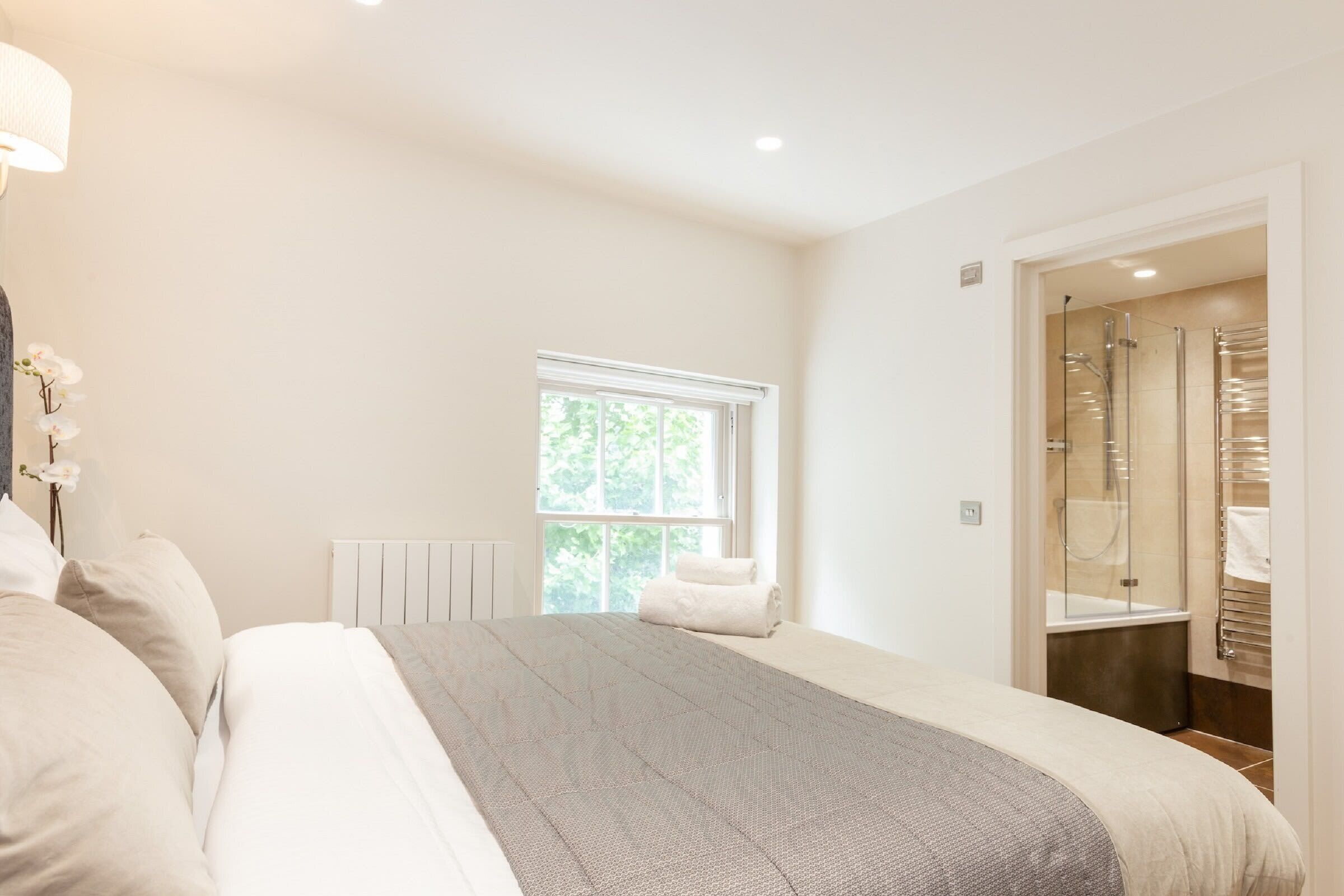 A bedroom with a bed, a window, and a bathroom with a shower and towel rack.