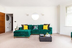 A living room with a green sectional sofa, a round mirror, and a small side table with a plant. - Spacious Talbot Woods Retreat | 2 En-Suites | Free Parking |25 min walk to Beach (Bournemouth)