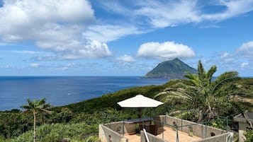 Um terraço com mesa e cadeiras, com vista para uma paisagem verdejante e o oceano.