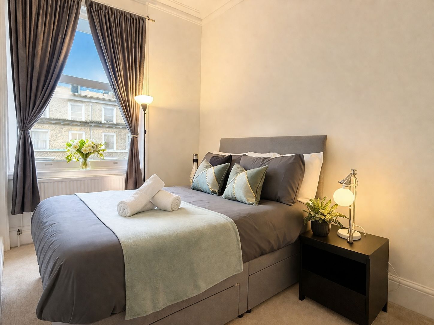 Een hotelkamer met een bed, nachtlampjes, een nachtkastje en een raam met gordijnen.