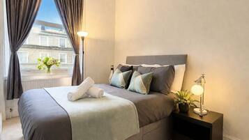 A hotel room with a bed, bedside lamps, a nightstand, and a window with curtains.