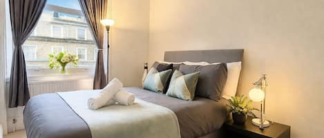 A hotel room with a bed, bedside lamps, a nightstand, and a window with curtains.