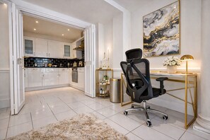 Une cuisine moderne avec des meubles blancs et un plan de travail noir, une chaise de bureau noire, un bureau doré et une œuvre d’art en marbre accrochée au mur.