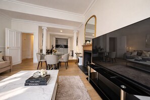 A modern living room with a flat-screen TV, a fireplace, a dining area, and a kitchen in the background. - Knightsbridge & South Kensington 2 Bed,2 Bath with Private Garden Near Hyde Park (London)