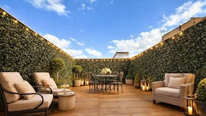 Une terrasse extérieure dotée d’une plateforme en bois, entourée d’un mur de verdure, avec des sièges et une table décorée de bougies.
