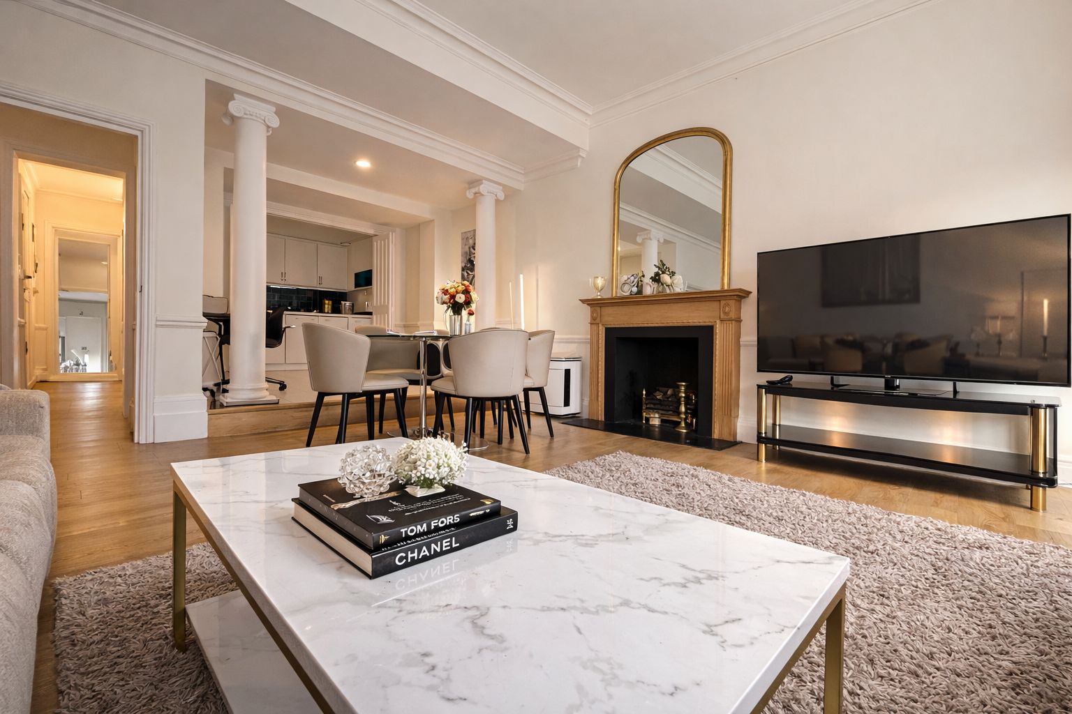 A modern living room with a marble coffee table, a fireplace, a TV, and a dining area with chairs.