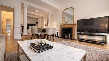 A modern living room with a marble coffee table, a fireplace, a TV, and a dining area with chairs.