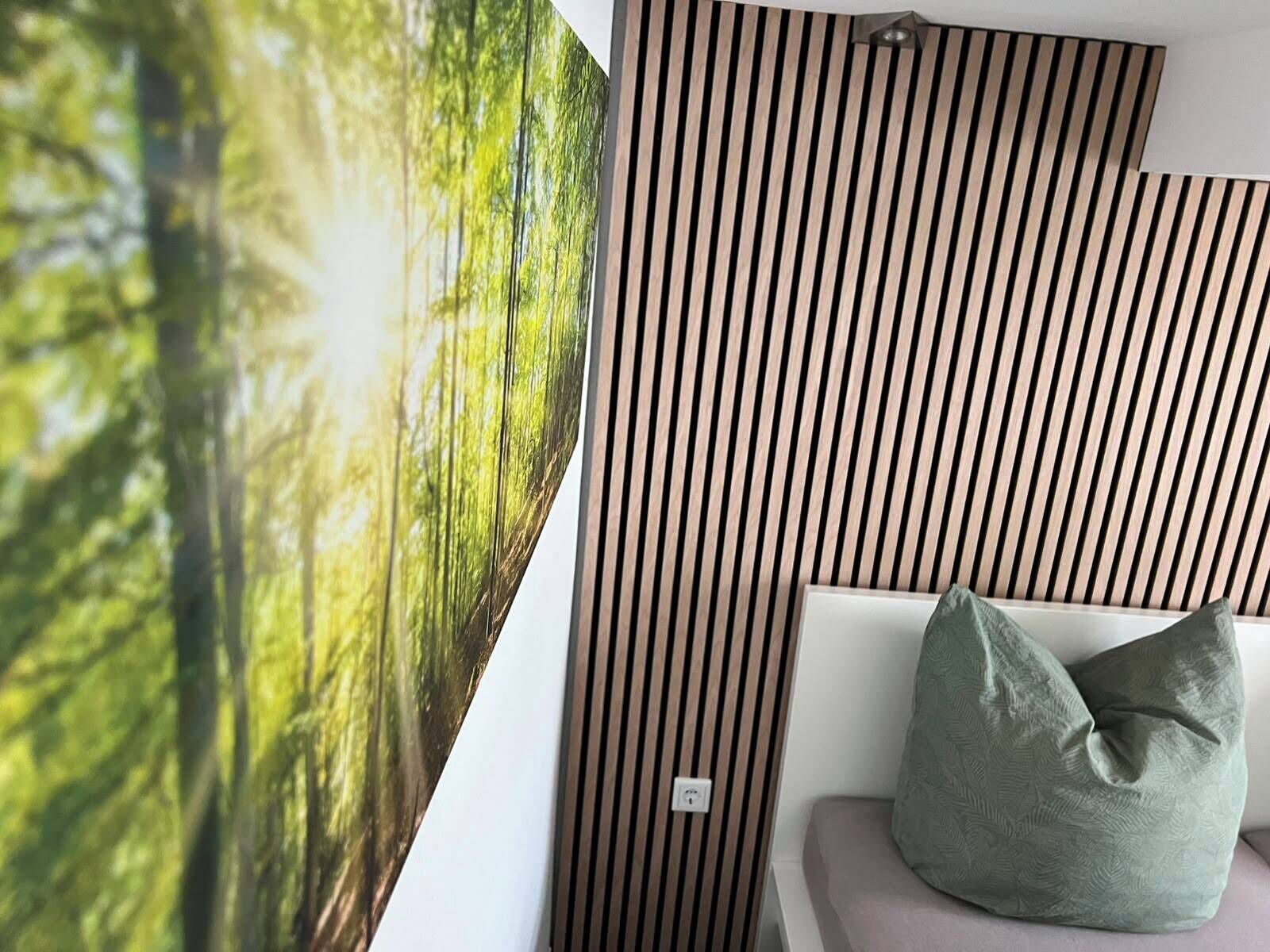 Une pièce avec un mur décoré de lambris, un coussin vert sur un canapé blanc et une grande affiche représentant une scène de forêt.
