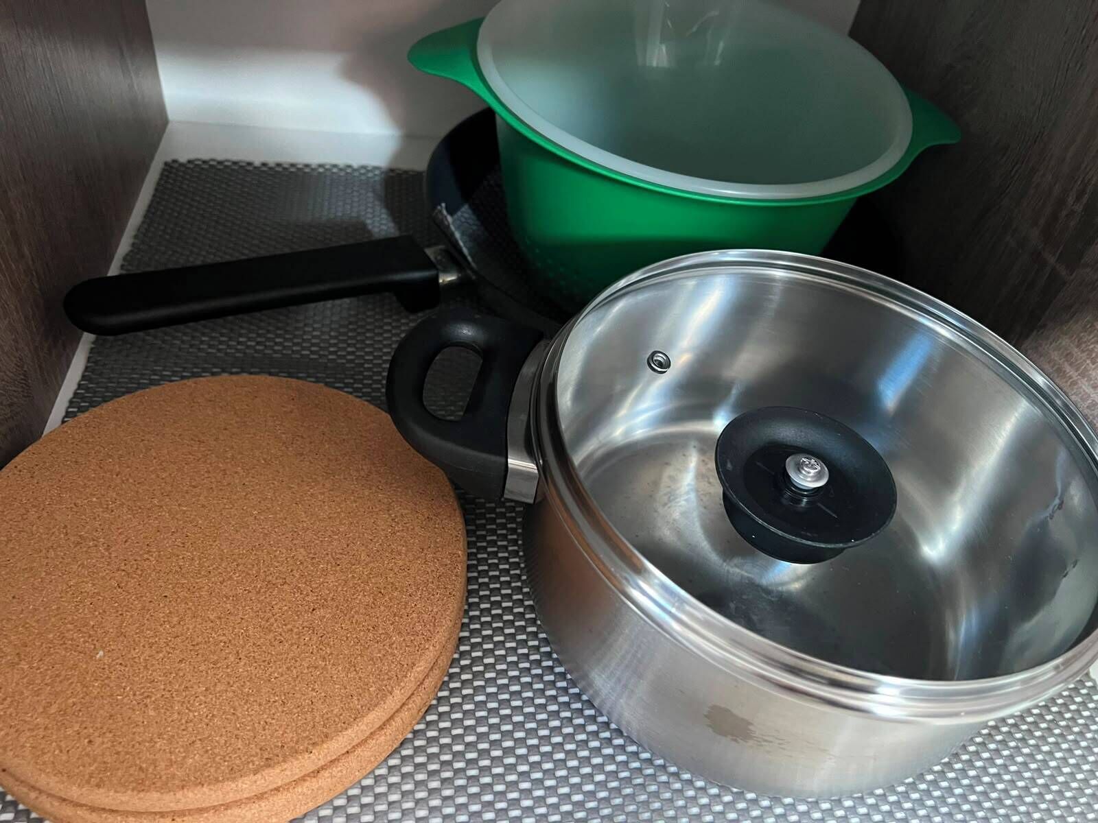 Un angolo cottura con una pentola in acciaio inox, una pentola verde con coperchio e un tappetino di sughero.