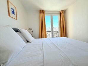 A hotel room with a bed, a nightstand, a lamp, a framed picture on the wall, and a window with curtains.
