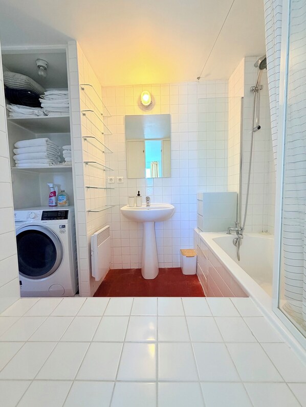 A bathroom with a washing machine, a sink, a mirror, and a shower.