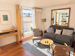 A living room with a sofa, a coffee table, a chair, a floor lamp, and a large mirror. - 1 BR Upper Marais with A/C (Paris)