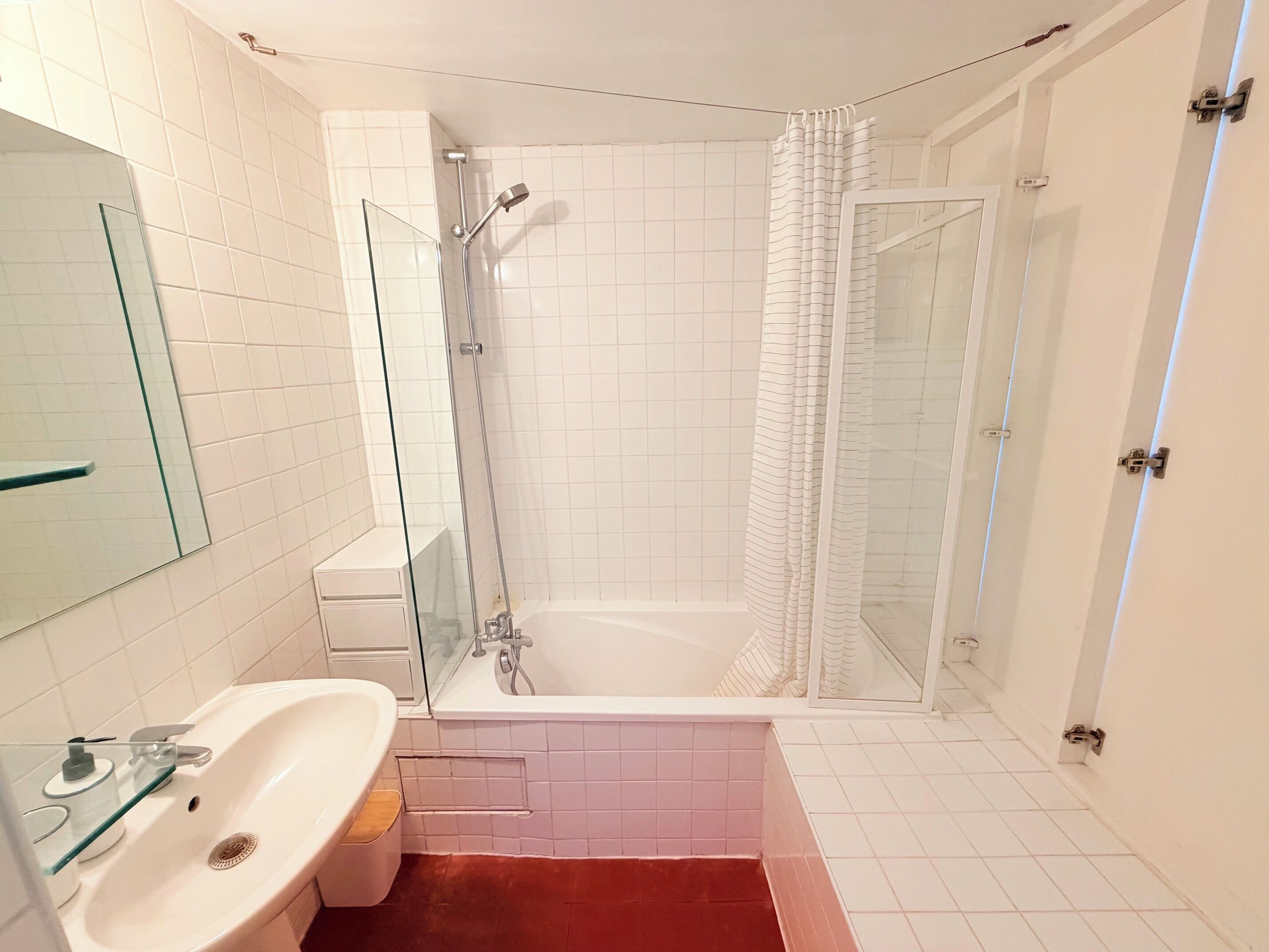 Ein Badezimmer mit Duschkabine aus Glas, einer weißen Badewanne und einem Waschbecken mit Glastrennwand.
