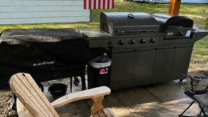 An outdoor patio with a grill, a wooden Adirondack chair, and an American flag.