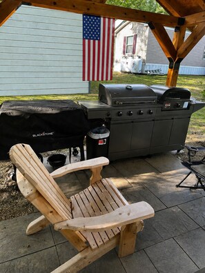 An outdoor patio with a grill, a wooden Adirondack chair, and an American flag.