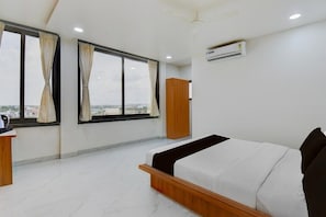 Une chambre d’hôtel équipée d’un lit, d’un bureau, d’une fenêtre avec des rideaux et d’un appareil de climatisation.