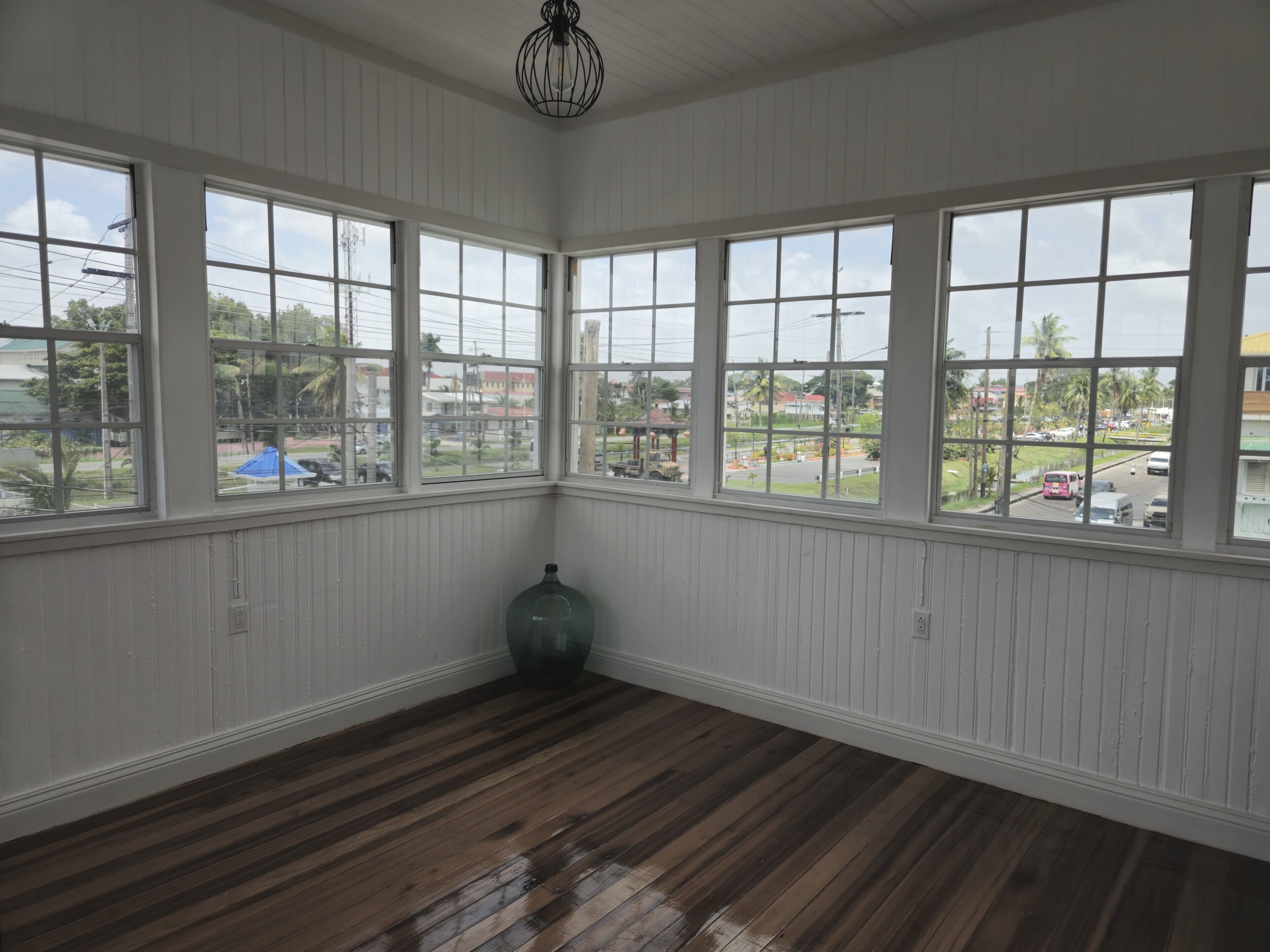 A room with large windows, wooden flooring, and a single green bottle.