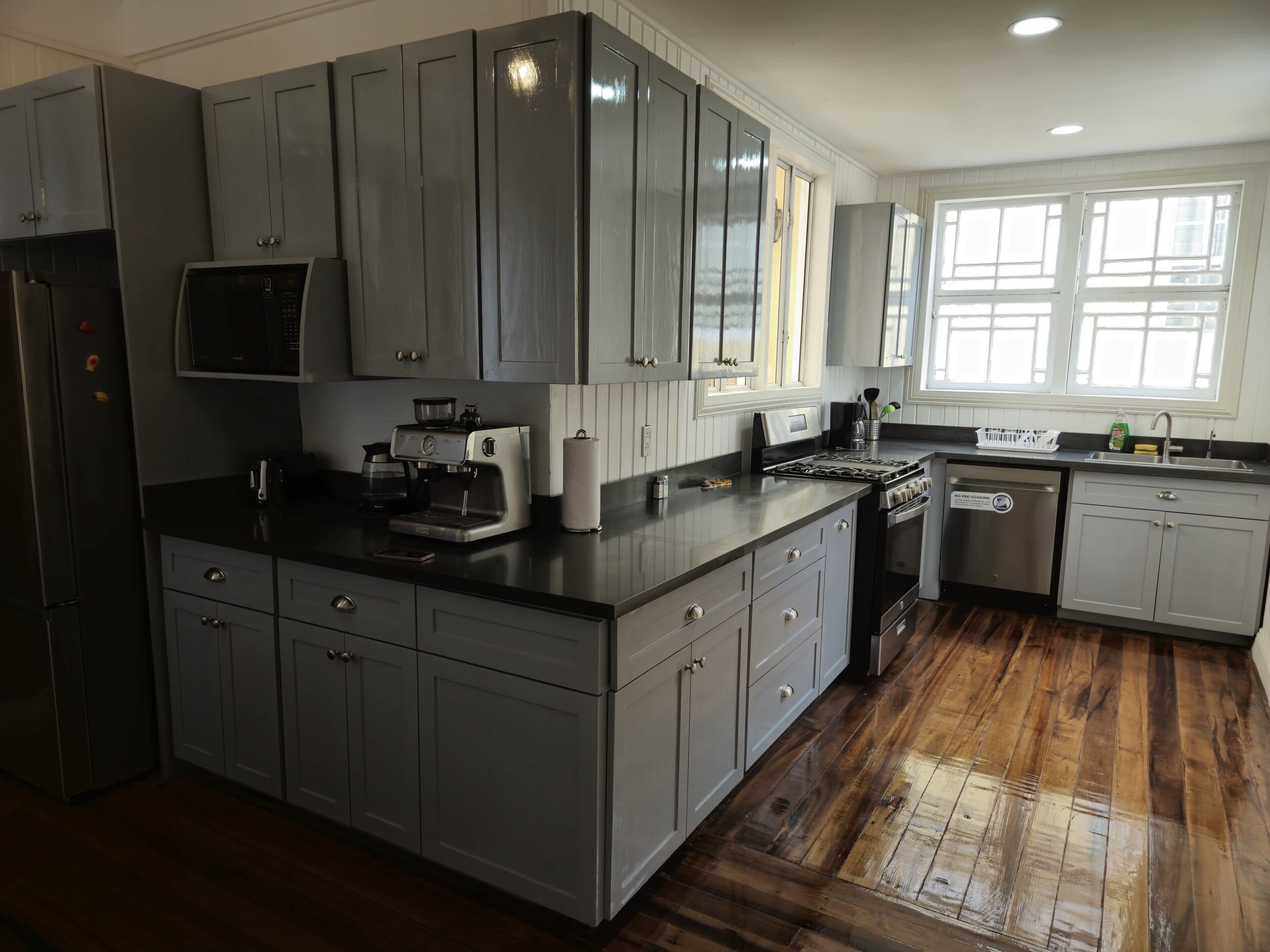 A kitchen with grey cabinets, a built-in microwave, a coffee maker, and a dishwasher.